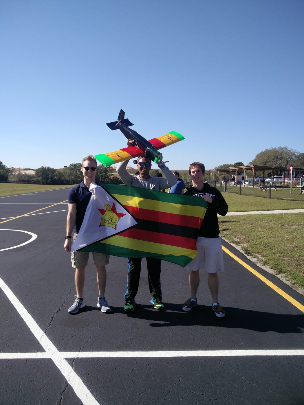 Mehul Patel holding up a model aircraft painted in Zimbabwe's colors behind a Zimbabwean flag